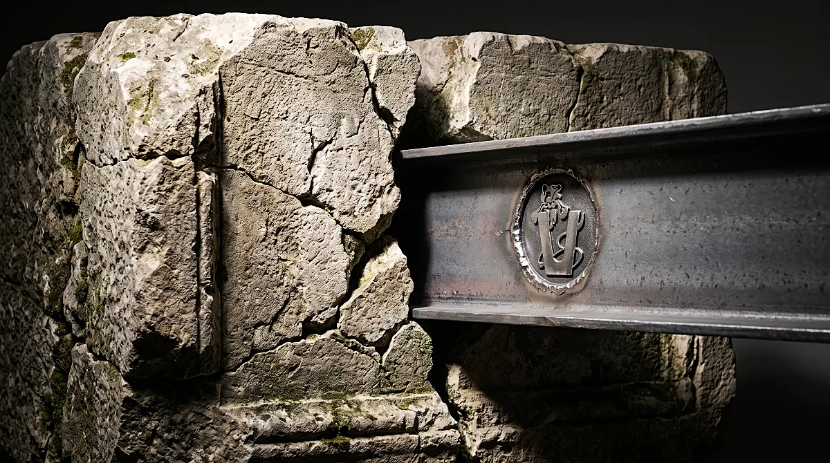 Massive ancient stone block deeply fractured by a solid forged steel beam with Vana logo physically stamped into the metal