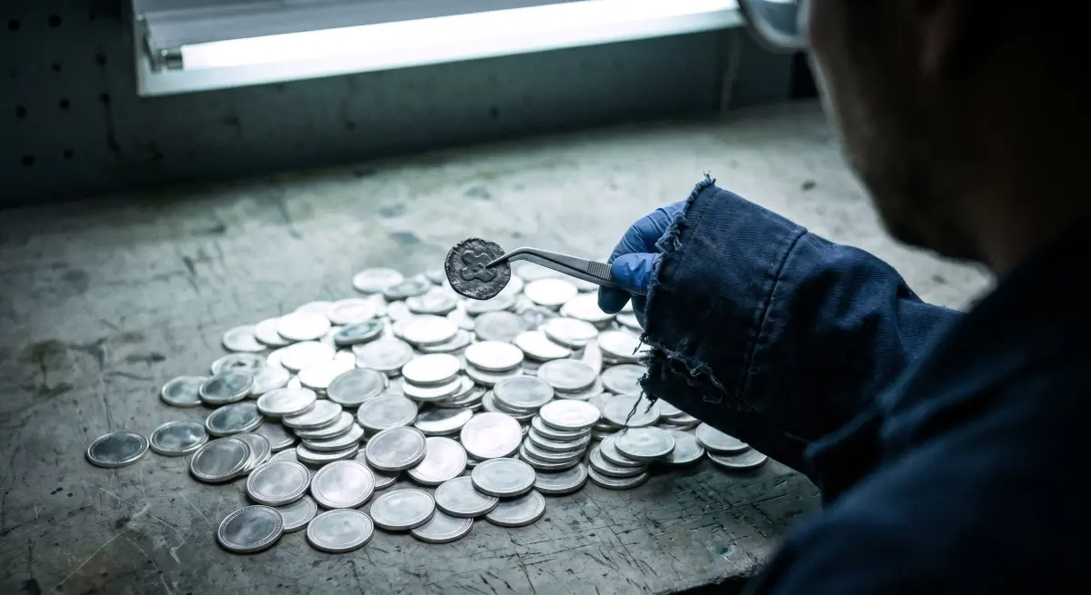A raw, documentary-style forensic photo showing a hand using metal tweezers to extract a distorted, fake cryptocurrency coin from a massive pile of clean tokens, illustrating the hidden crypto token scam.